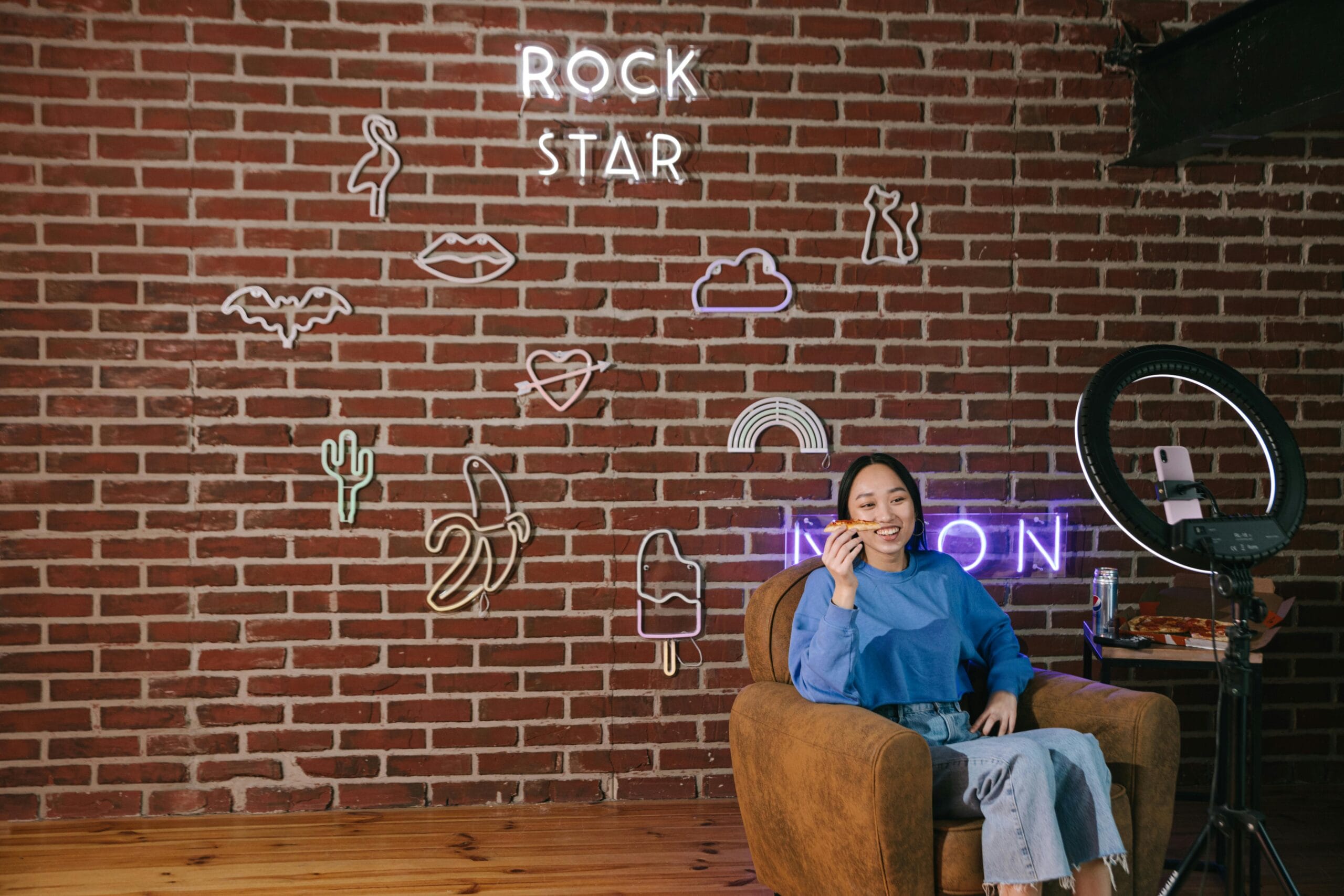 Asian woman streaming content with neon signs on a brick wall. Modern influencer setup.